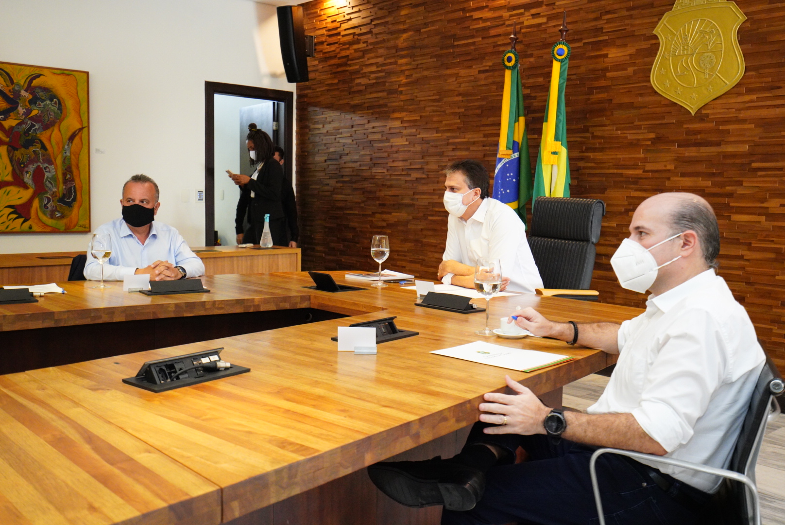 ministro, governador e prefeito sentados ao redor de mesa, usando máscara e conversando